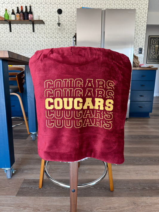 A Maroon blanket with sherpa backing and gold cougars design over the back of a chair.