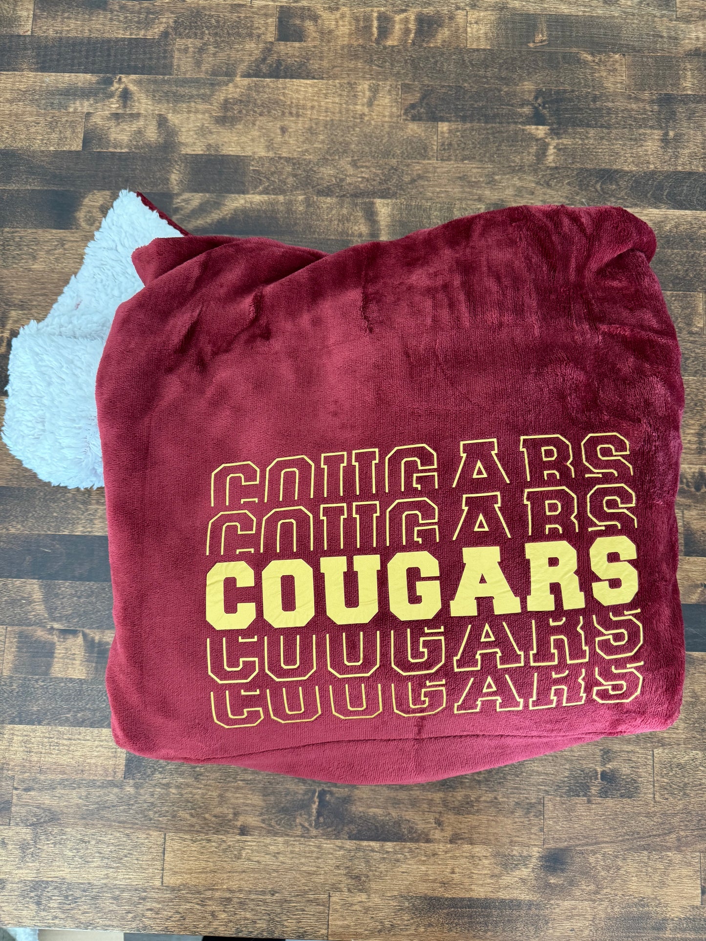 A folded maroon blanket with gold cougars design