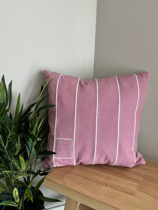 Photo of a pink pillow with white vertical strip that says Uff Da in a box on the lower right side of the pillow